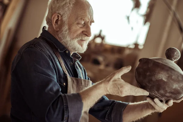 Старший гончар в фартуке рассматривает керамическую миску в мастерской — Stock Photo