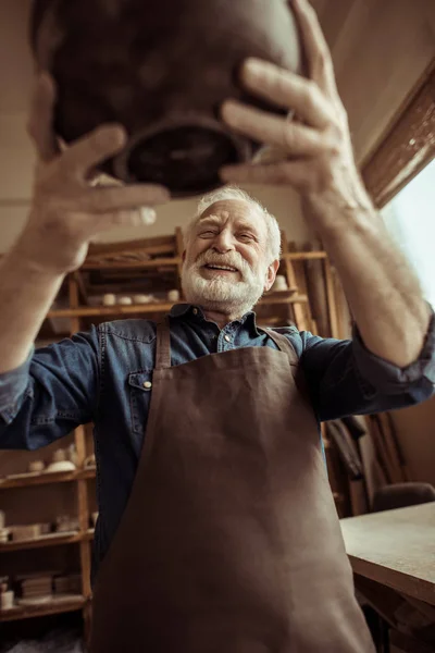 Alfarero senior en delantal examinando tazón de cerámica en el taller — Stock Photo