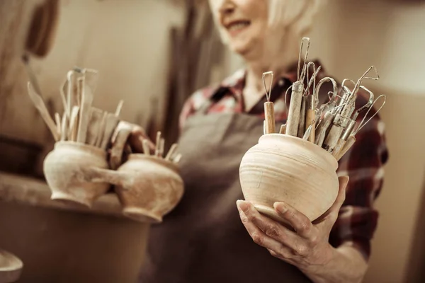 Mujer mayor sosteniendo cuencos con herramientas de cerámica en el taller - foto de stock