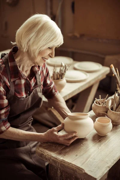 Female potter sitting at table and examining ceramic bowl at workshop — Stock Photo