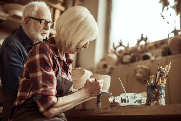 Mujer pintando olla de barro con alfarero senior en el taller - foto de stock