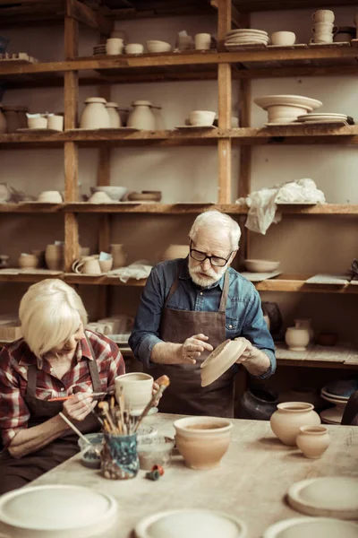 Woman painting clay pot with senior potter at workshop — Stock Photo