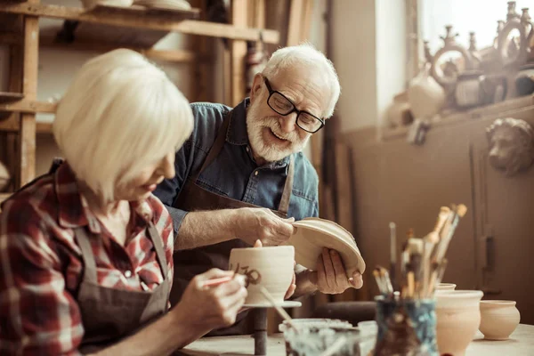 Женщина рисует глиняный горшок со старшим гончаром в мастерской — стоковое фото