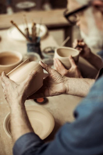 Close up of senior potter in apron and eyeglasses examining ceramic bowl — Stock Photo