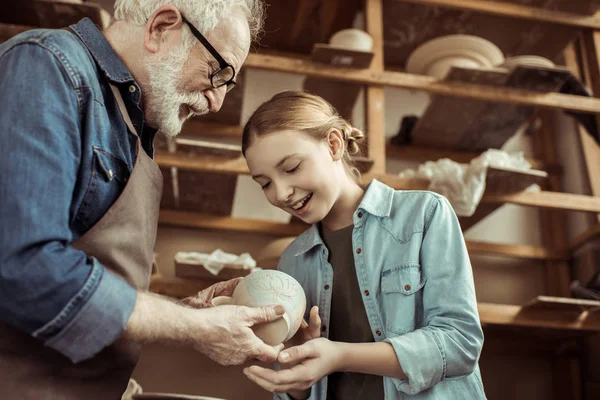 Granddaughter and grandfather holding and examining clay goods — Stock Photo