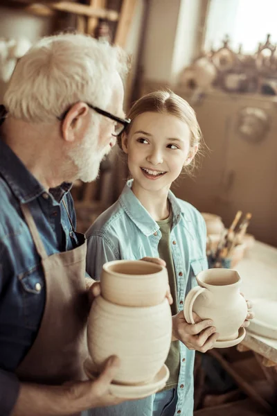 Petite-fille et grand-père tenant et examinant des marchandises en argile — Photo de stock