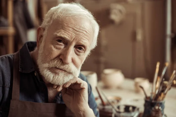 Portrait de potier sénior assis à table et regardant la caméra — Photo de stock