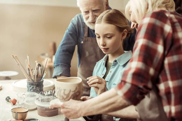 Side view of girl painting clay pot and grandparents helping at workshop — Stock Photo