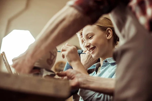 Close up de menina pintando panela de barro e avós ajudando na oficina — Fotografia de Stock