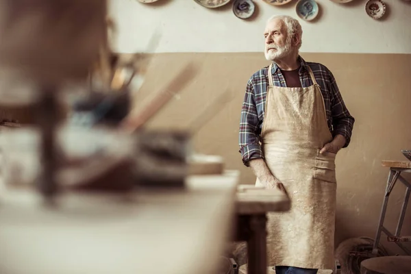 Vue de face du potier senior dans le tablier debout à l'atelier — Photo de stock