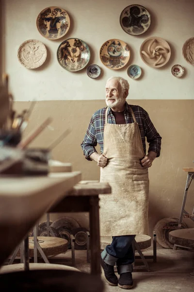 Front view of senior potter in apron standing at workshop — Stock Photo