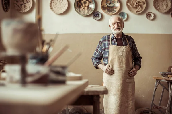 Front view of senior potter in apron standing at workshop — Stock Photo