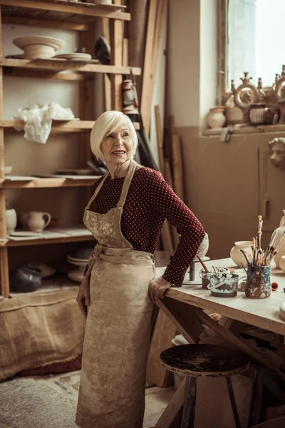 Вид спереди женщины-гончара в фартуке, стоящей в мастерской — стоковое фото