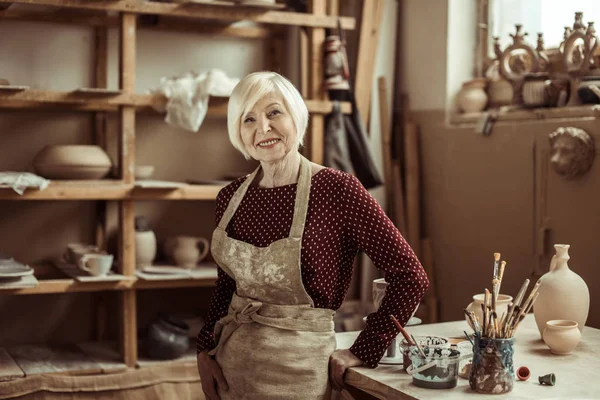 Вид спереди женщины-гончара в фартуке, стоящей в мастерской — стоковое фото