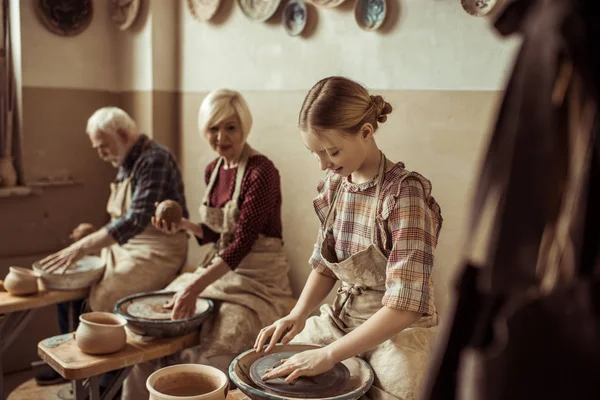 Abuela y abuelo con nieta haciendo cerámica en el taller - foto de stock