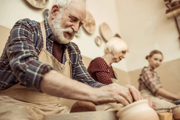 Abuela y abuelo con nieta haciendo cerámica en el taller - foto de stock