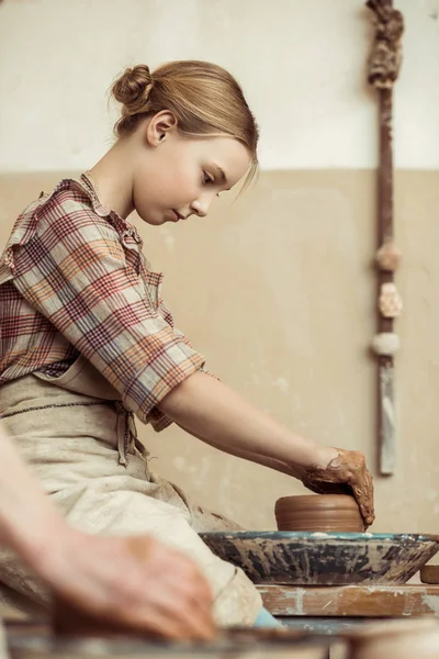 Вид сбоку маленькой девочки, делающей керамику на колесе в мастерской — стоковое фото
