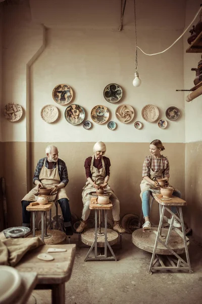 Abuela y abuelo con nieta haciendo cerámica en el taller - foto de stock