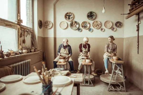 Abuela y abuelo con nieta haciendo cerámica en el taller - foto de stock