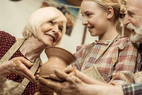 Grand-mère et grand-père avec petite-fille tenant vase d'argile dans l'atelier — Photo de stock