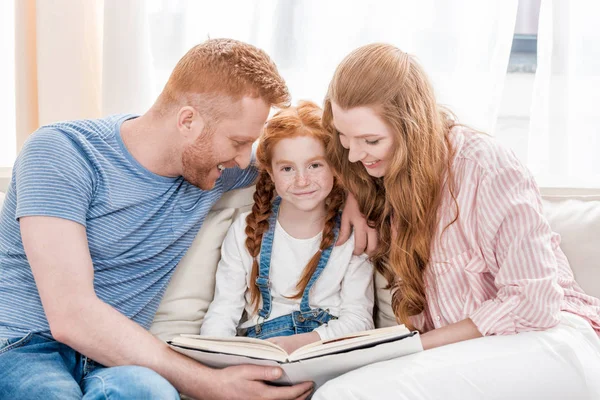 Padres con hija leyendo libro - foto de stock