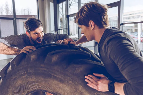 Hombres tirando de neumático juntos - foto de stock