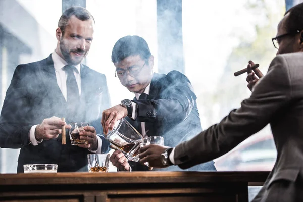 Equipo de negocios multicultural pasar tiempo, fumar cigarros y beber whisky - foto de stock