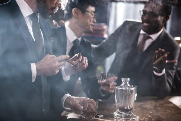 Команда мультикультурного бизнеса проводит время, курит сигары и пьет виски — стоковое фото