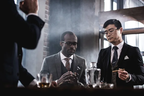 Equipo de negocios multicultural pasar tiempo, fumar cigarros y beber whisky - foto de stock