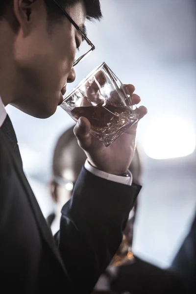 Primer plano vista de asiático hombre de negocios en gafas beber whisky de vidrio - foto de stock