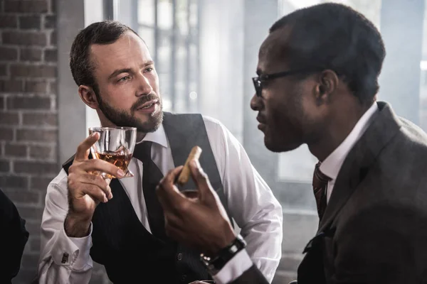 Dos hombres confiados con cigarro y vaso de bebida alcohólica hablando - foto de stock