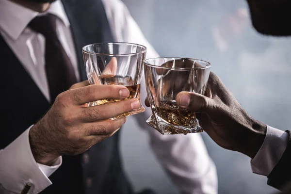 Close-up partial view of two men in formal wear clinking whiskey glasses — Stock Photo