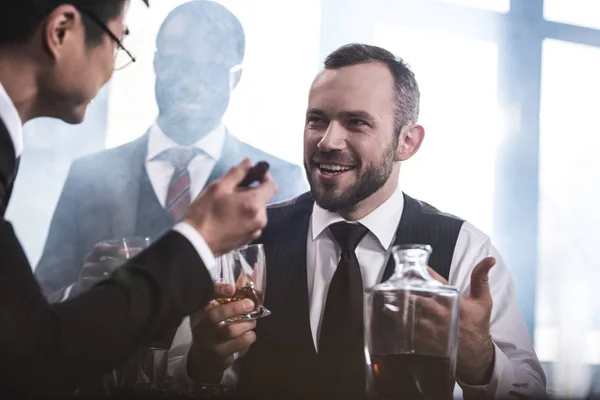 Grupo multiétnico de empresarios que fuman y beben whisky en el interior, reunión del equipo empresarial - foto de stock