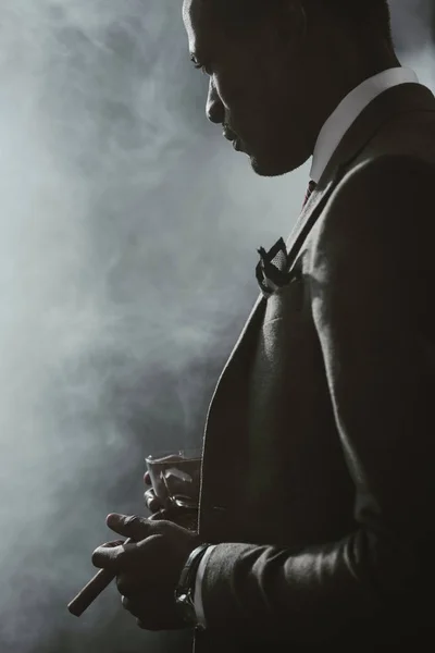 Confident african american businessman in suit with glass of whiskey smoking cigar — Stock Photo