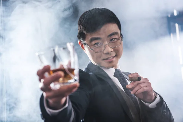Primer plano vista de seguro asiático hombre de negocios beber whisky y fumar cigarro - foto de stock