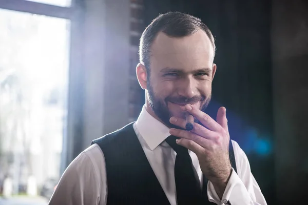 Gros plan portrait d'un bel homme souriant et confiant fumant du cigare à l'intérieur — Photo de stock