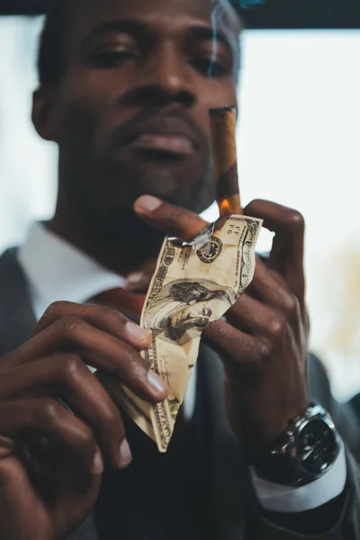 Confident african american businessman smoking cigar and burning dollar banknote — Stock Photo
