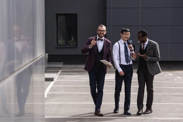 Sorrindo equipe de negócios multicultural andando na rua perto de edifício de escritório moderno — Fotografia de Stock