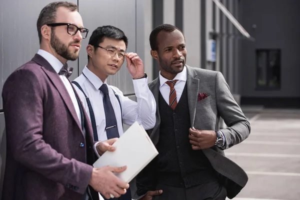 Retrato de equipo de negocios multicultural confiado de pie cerca de la oficina y mirando a un lado - foto de stock