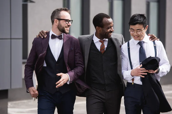 Jeunes hommes d'affaires multiethniques élégants en tenue de cérémonie marchant à l'extérieur, réunion de l'équipe d'affaires — Photo de stock