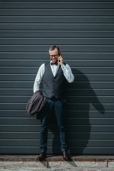 Hombre de negocios con estilo y confianza utilizando el teléfono inteligente y posando al aire libre en la pared - foto de stock