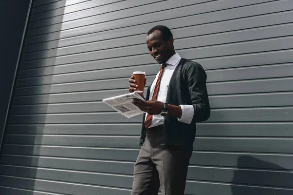 Stylish african american businessman reading newspaper and holding coffee to go outdoors — Stock Photo