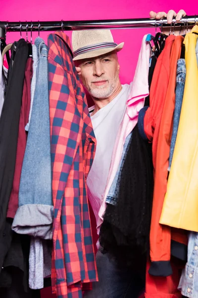 Старший чоловік з різноманітним одягом на вішаках — стокове фото