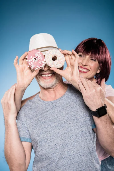 Elderly couple fooling around with doughnuts — Stock Photo