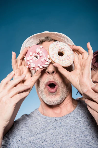 Elderly couple fooling around with doughnuts — Stock Photo