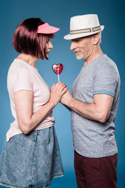 Elderly couple holding hands with lollipop — Stock Photo