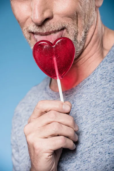 Man licking lollipop in form of heart — Stock Photo