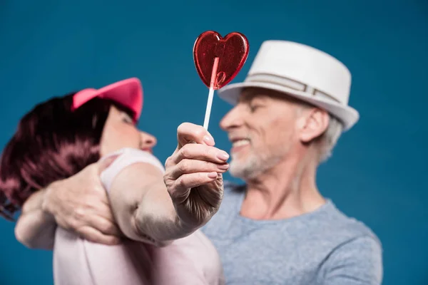 Elderly couple hugging and holding lollipop — Stock Photo