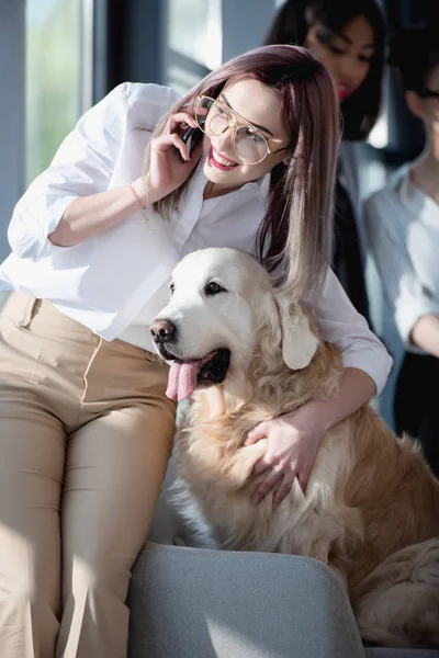 Businesswoman talking on smartphone and hugging dog — Stock Photo