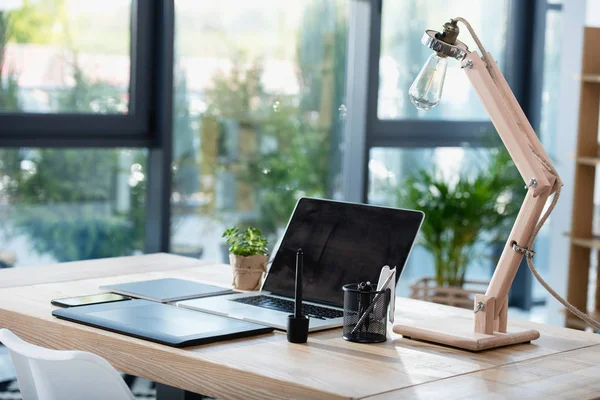 Laptop com tablet gráfico e lâmpada no local de trabalho — Fotografia de Stock